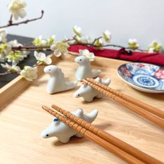 four small white rabbits with chopsticks on a wooden tray next to some flowers