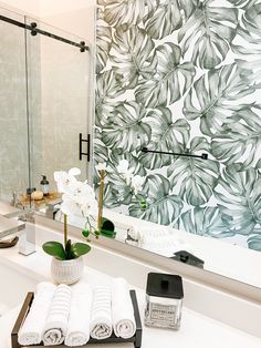 a bathroom sink with towels on it next to a large mirror and flowers in a vase