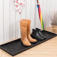 three pairs of rubber boots and an umbrella on a black mat in front of a white wall