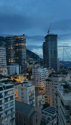 the city skyline is lit up at night with skyscrapers in the foreground and mountains in the background