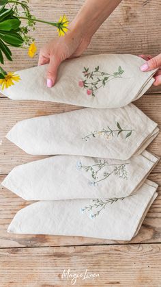 four napkins with embroidered flowers on them are being held by a woman's hand