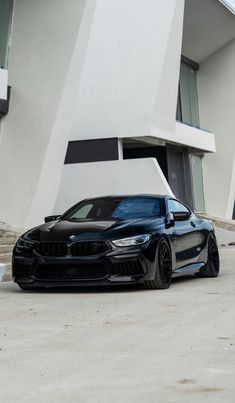 a black bmw car parked in front of a white building with stairs leading up to it