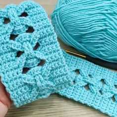 a crocheted pair of blue gloves next to a ball of yarn