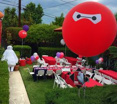 a large red balloon sitting on top of a lush green field next to tables and chairs