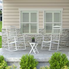 three white rocking chairs sitting on top of a cement slab next to a stone wall