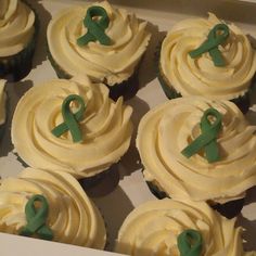 cupcakes with white frosting and green ribbons in a box