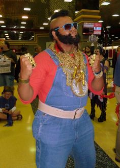 a man in overalls and sunglasses holding up two wine glasses with chains around his neck