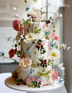 a three tiered white cake with flowers on it's side and the top layer is covered in icing