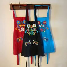 three aprons hanging on a wall with flowers and tassels attached to them