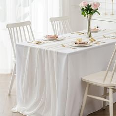 the table is set with white chairs and place settings for two people to sit at