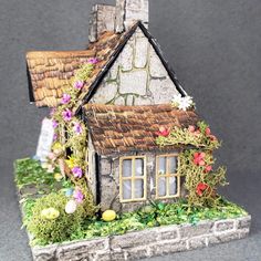 a miniature house with flowers and vines on the roof is shown in front of a gray background