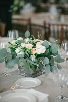 a vase filled with white flowers sitting on top of a table next to wine glasses