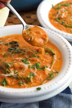 a spoon full of soup being held up by two plates with another bowl in the background