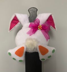 a white stuffed animal sitting on top of a black stand with a pink bow around its neck