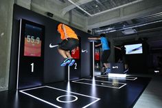 two people jumping over obstacles in an indoor area with nike advertisement on the wall behind them