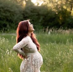 a pregnant woman standing in tall grass with her hands on her hips looking up at the sky