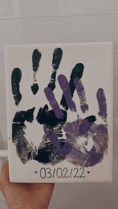 a person holding up a handprint with purple and black paint on it in front of a white wall