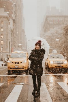 a woman is walking across the street in the snow with an umbrella over her head