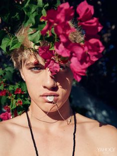 a young man with flowers on his head is posing in front of some pink flowers