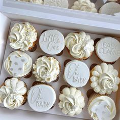 twelve cupcakes in a box with white frosting and baby ones on them