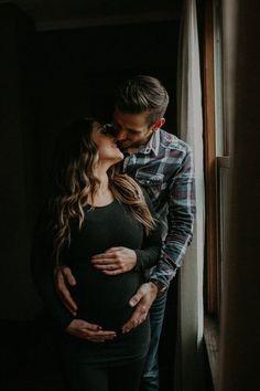 a pregnant couple kissing in front of a window