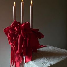 three candles are lit on top of a cake with red ribbons and bows around it