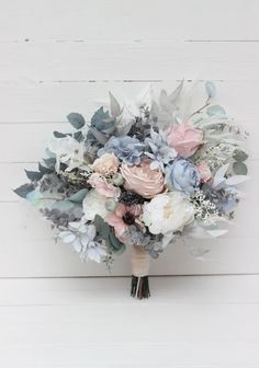 a bridal bouquet with blue, pink and white flowers on a wooden surface in front of a white plank wall