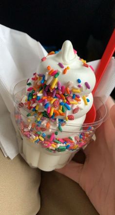 a person holding a plastic cup filled with ice cream and sprinkles on top