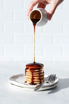 someone is pouring syrup on top of a stack of pancakes that are sitting on a plate