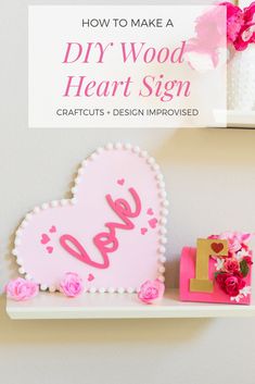 a heart shaped sign sitting on top of a shelf next to flowers and a vase