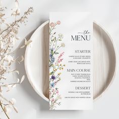 a white plate with a menu on it next to some dried flowers and a plant