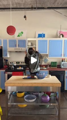 a woman standing in a kitchen next to a table with bowls and plates on it