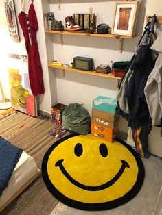 a yellow smiley face rug sitting on top of a floor next to a shelf filled with clothes