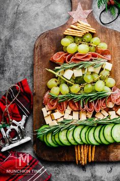 a wooden cutting board topped with cucumbers, cheese and crackers next to a christmas tree shaped platter