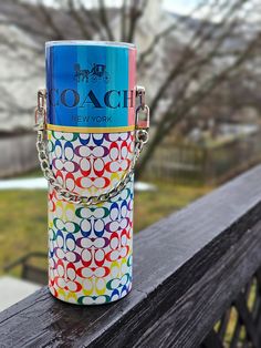 a colorful coach purse sitting on top of a wooden rail next to a tree in the background