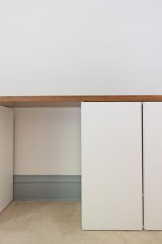 an empty room with two white cupboards and a wooden shelf above the closet door