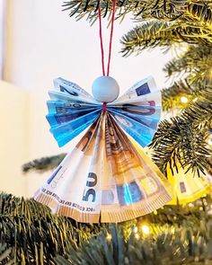 an ornament made out of money hanging from a christmas tree with lights in the background