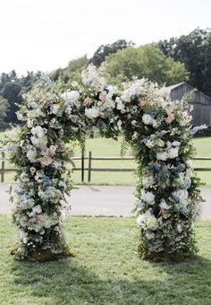 an arch made out of flowers and greenery in front of a barn with a wooden fence