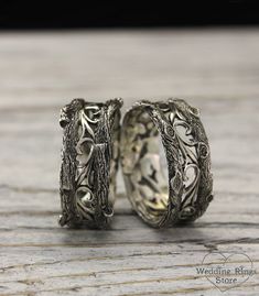 two wedding rings made out of silver with vines and leaves on the sides, sitting on a wooden surface