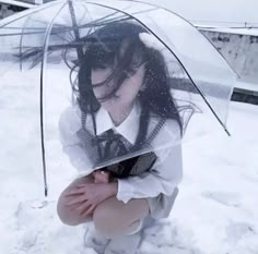 a woman kneeling in the snow with an umbrella over her head and hands on her knees