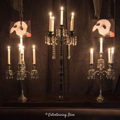 candles with masks on them are lit in front of a black curtained wall and chandelier