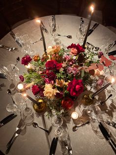 a centerpiece with candles and flowers on a white table cloth surrounded by silverware