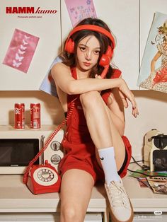 a young woman sitting on top of a counter next to a red phone and headphones