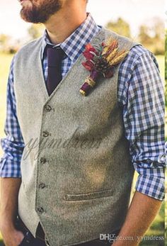 a man wearing a vest and tie with a flower on his lapel, standing in the grass