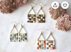 three pairs of earrings sitting on top of a white table next to some pink flowers