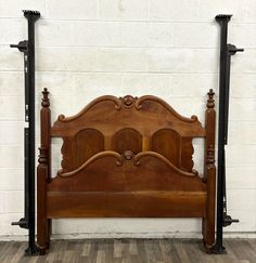 an antique wooden bed frame against a white brick wall with two black metal posts on each side