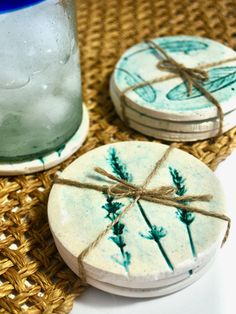 three coasters with blue and green designs on them sitting next to a glass jar