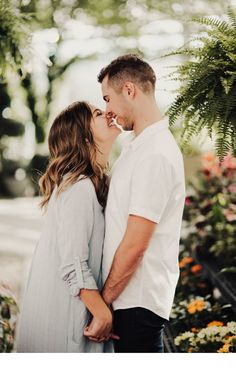 a man and woman standing next to each other in front of flowers with their noses close together