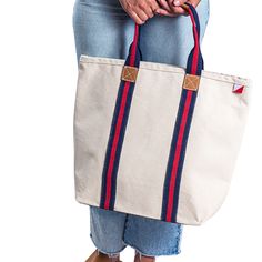 Our Society Tote bag is an instant classic. Striped cotton webbing highlight the bag from bottom to top. A full leather bottom protects your bag and the crisp heavyweight natural canvas gives this bag a lot of structure. A super chic everyday bag. This item can be monogramed!Product Overview: Dimensions: 20" x 15" x 5" Crafted with heavyweight cotton canvas Nubuck leather details on the strap and full bottom Metal stud detail Interior pocket The monogrammed items are custom-made to order and can Canvas Weekender Bag With Canvas Lining For Shopping, Navy Bags With Leather Trim For Everyday Use, Navy Bag With Leather Trim For Everyday, Cotton Travel Bags With Twill Lining, Natural Canvas Bags With Canvas Lining, Classic Cotton Shoulder Bag For Everyday, Cream Bags With Canvas Lining For Everyday Use, Navy Canvas Bag With Adjustable Strap, Cream Coated Canvas Everyday Bag