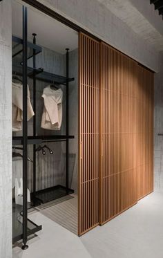 an open closet with wooden doors and clothes hanging on the shelves in front of it